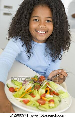 Stock Image - Young girl in kitchen eating salad smiling. Fotosearch