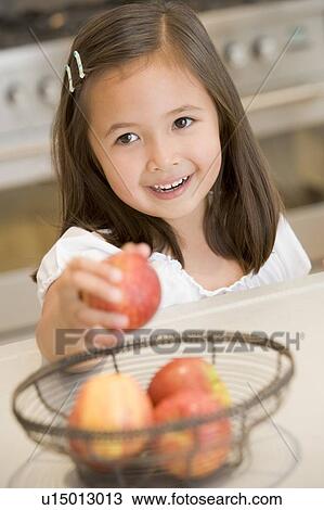 Young girl in kitchen getting apple off counter smiling View Large Photo Image Stock Image - Young girl in kitchen getting apple off counter smiling. Fotosearch