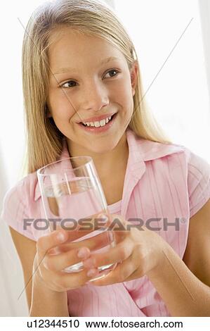 Stock Image - Young girl indoors drinking water smiling. Fotosearch