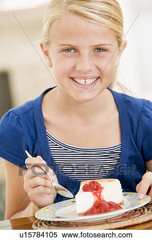 Stock Photography - Young girl indoors eating cheesecake smiling. Fotosearch