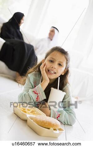 Young girl with fast food in living room smiling with parents in background (high key/selective focus) View Large Photo Image Stock Photo - Young girl with fast food in living room smiling with parents in background (high key/selective focus). Fotosearch