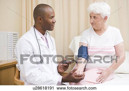 Stock Image - Doctor checking woman's blood pressure in exam room. Fotosearch