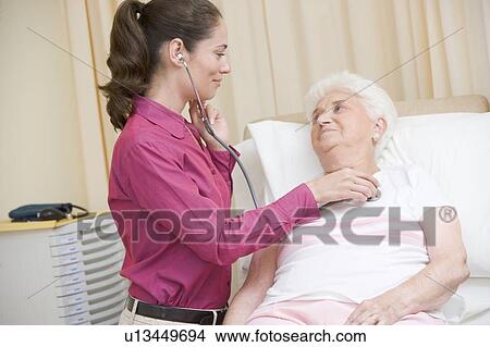 Picture - Doctor giving checkup with stethoscope to woman in exam room smiling. Fotosearch