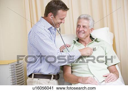 Stock Image - Doctor giving man checkup with stethoscope in exam room smiling. Fotosearch