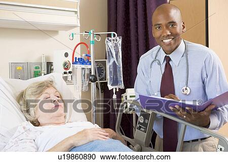 Stock Image - Doctor Making Notes About Senior Woman Lying In Hospital Bed. Fotosearch