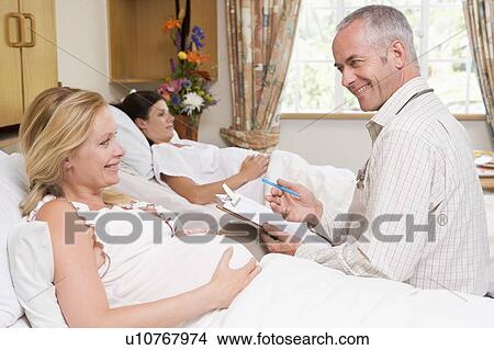 Picture - Doctor talking to pregnant woman holding chart and smiling. Fotosearch