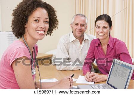 Stock Image - Doctor with laptop and couple in doctor's office smiling. Fotosearch