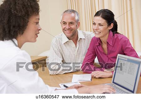 Stock Photo - Doctor with laptop and couple in doctor's office smiling. Fotosearch