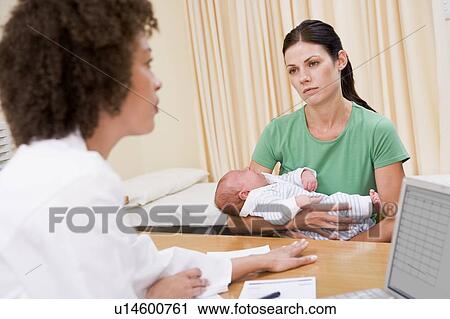 Stock Image - Doctor with laptop and woman in doctor's office holding baby. Fotosearch