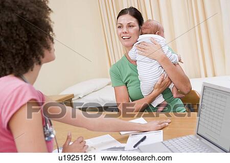 Stock Image - Doctor with laptop and woman in doctor's office holding baby. Fotosearch