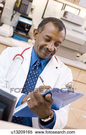 Stock Photography - A Doctor Writing On A Clipboard At The Reception Area Of A Hospital. Fotosearch