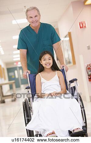 Stock Image - An Orderly Pushing A Little Girl In A Wheelchair Down A Hospital Corridor. Fotosearch