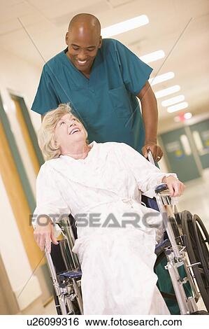 Stock Photograph - An Orderly Pushing A Senior Woman In A Wheelchair Down A Hospital Corridor. Fotosearch
