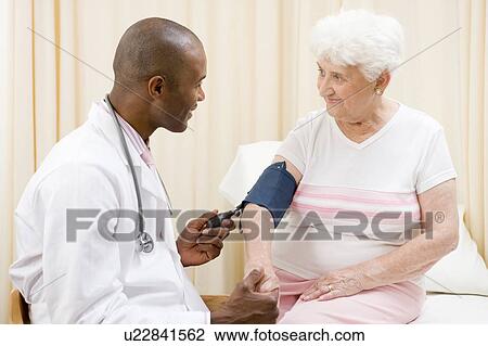 Doctor checking woman's blood pressure in exam room smiling View Large Photo Image Stock Image - Doctor checking woman's blood pressure in exam room smiling. Fotosearch