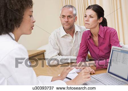 Stock Photo - Doctor with laptop and couple in doctor's office frowning. Fotosearch