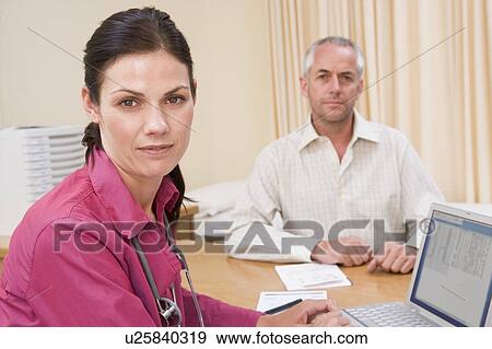 Stock Photo - Doctor with laptop and man in doctor's office frowning. Fotosearch