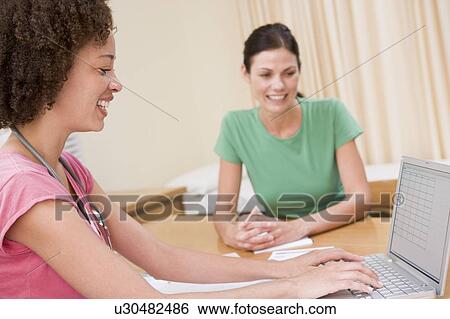 Stock Photograph - Doctor with laptop and woman in doctor's office smiling. Fotosearch