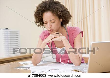 Stock Image - Doctor with laptop reading in doctor's office. Fotosearch