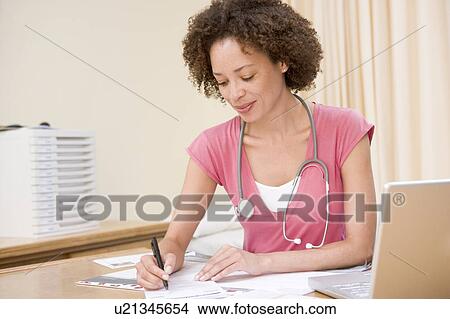 Picture - Doctor with laptop writing in doctor's office. Fotosearch