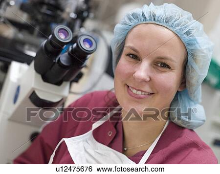 Stock Photograph - Embryologist sitting by microscope smiling (selective focus). Fotosearch