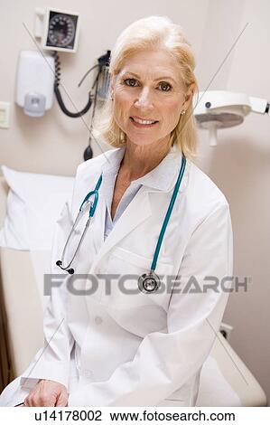 Stock Image - Middle Aged Female Doctor Sitting In A Hospital Ward. Fotosearch
