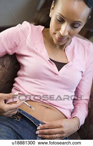 Stock Image - Woman injecting drugs to prepare for IVF treatment. Fotosearch