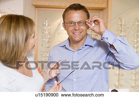 Stock Image - Couple trying on eyeglasses at optometrists smiling. Fotosearch