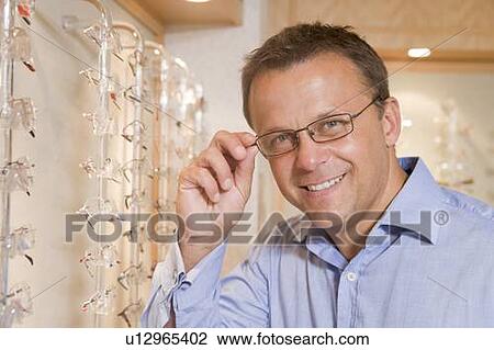 Stock Image - Man trying on eyeglasses at optometrists smiling. Fotosearch