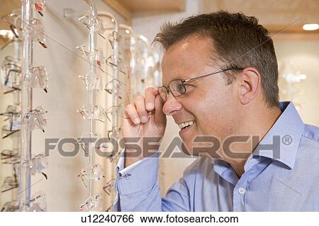 Stock Photograph - Man trying on eyeglasses at optometrists smiling. Fotosearch