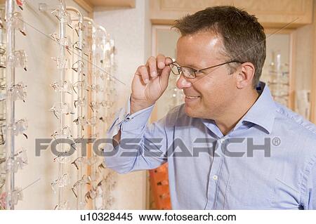 Stock Photography - Man trying on eyeglasses at optometrists smiling. Fotosearch