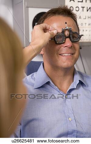 Stock Image - Optometrist in exam room with man in chair smiling. Fotosearch