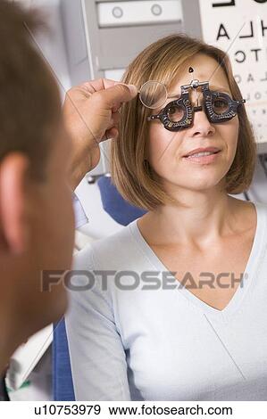Stock Photo - Optometrist in exam room with woman in chair. Fotosearch
