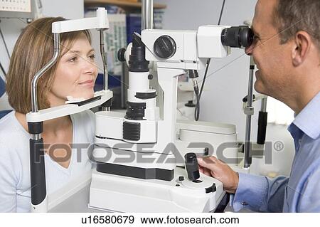 Stock Photo - Optometrist in exam room with woman in chair. Fotosearch