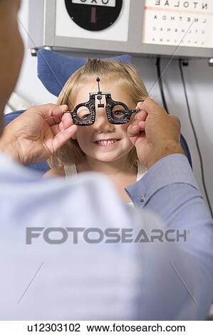 Stock Image - Optometrist in exam room with young girl in chair smiling. Fotosearch