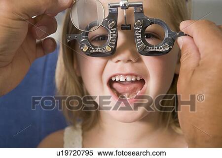 Stock Photography - Optometrist in exam room with young girl in chair smiling. Fotosearch