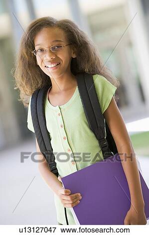 Stock Photo - Student standing outside school holding binder and smiling (selective focus). Fotosearch