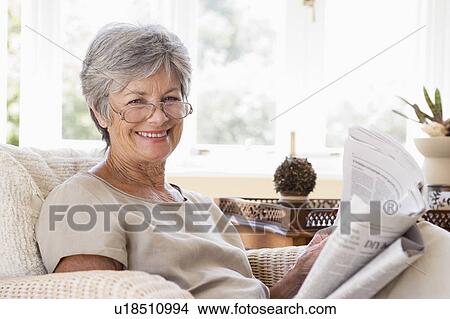 Picture - Woman in living room reading newspaper smiling. Fotosearch