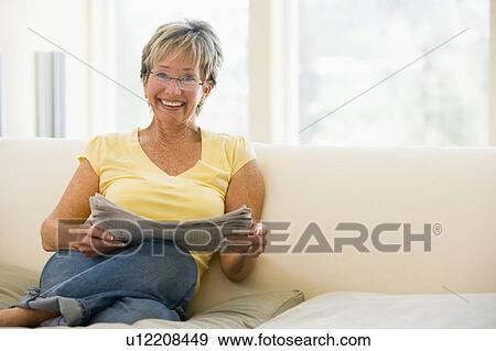 Stock Photo - Woman in living room reading newspaper smiling. Fotosearch