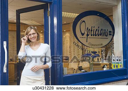 Stock Photo - Woman standing at front entrance of optometrists smiling. Fotosearch
