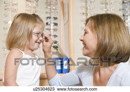 Woman trying eyeglasses on young girl at optometrists smiling View Large Photo Image Stock Image - Woman trying eyeglasses on young girl at optometrists smiling. Fotosearch