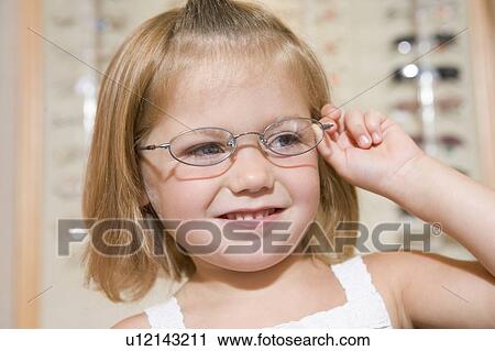 Stock Image - Young girl trying on eyeglasses at optometrists smiling. Fotosearch