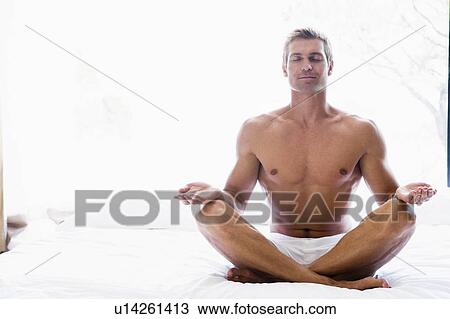 Stock Image - Man sitting on bed doing yoga. Fotosearch
