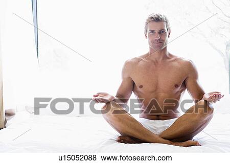 Stock Photo - Man sitting on bed doing yoga. Fotosearch