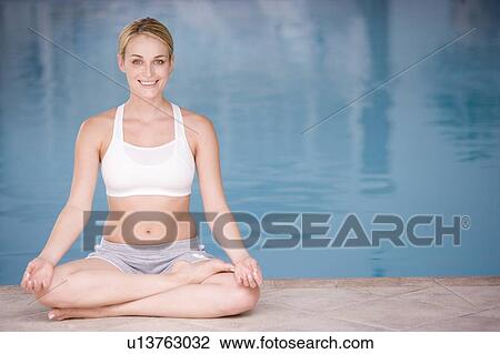 Stock Image - Woman sitting poolside doing yoga smiling. Fotosearch
