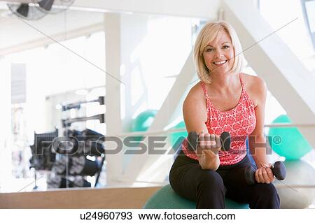 Stock Image - Woman Using Hand Weights On Swiss Ball At Gym. Fotosearch