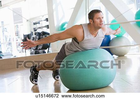 Stock Image - Man Balancing On Swiss Ball At Gym. Fotosearch