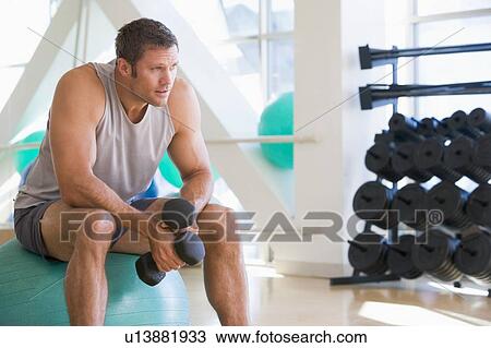 Stock Image - Man Using Hand Weights On Swiss Ball At Gym. Fotosearch