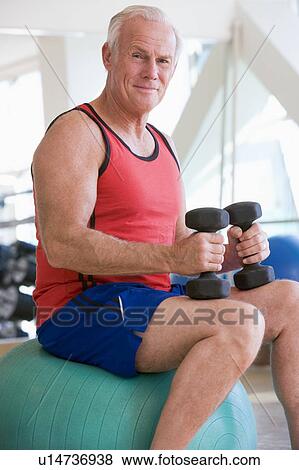 Stock Photo - Man Using Hand Weights On Swiss Ball At Gym. Fotosearch