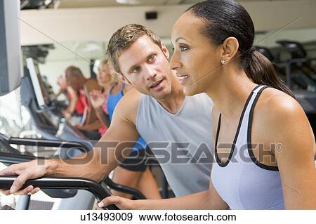 Stock Photo - Personal Trainer Encouraging Woman Using Treadmill At Gym. Fotosearch