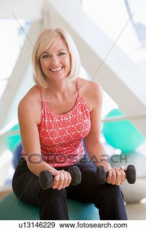 Stock Photo - Woman Using Hand Weights On Swiss Ball At Gym. Fotosearch